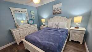 A bedroom with a large bed, two nightstands, a dresser, a ceiling fan, and a wall with framed artwork. - El Palmar Unit 2 Third Level from Beach (Indian Rocks Beach)