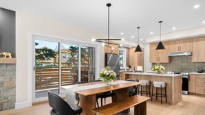 Una cocina moderna con una isla central, armarios de madera y un amplio ventanal que ofrece vistas a una casa y árboles.