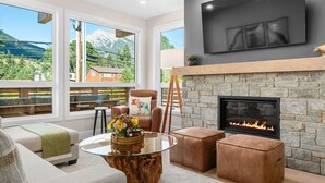 Una sala de estar moderna con chimenea de piedra, asientos cómodos y ventanas amplias que ofrecen vistas a las montañas.