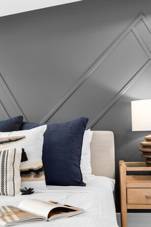 Una cama bien tendida con una colcha blanca y varios almohadones, incluyendo uno azul oscuro.