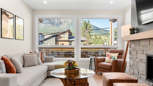 Una sala de estar moderna con sofá, sillón y mesa de centro, ventanas amplias con vistas a la montaña y una chimenea.