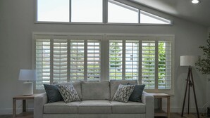 Ein Wohnzimmer mit einer Couch, einer Lampe und Blick durch große Fenster.