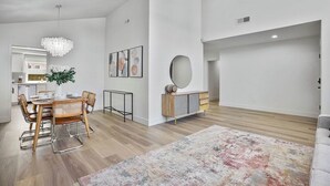 Ein modernes Wohnzimmer mit Essbereich, einem großen Spiegel und einer Deckenleuchte.