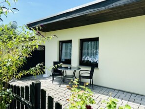 A patio with a table and chairs, a wooden fence, and a building with two windows. - F-1112 Vacation apartment Lobbe - Holiday apartment Lobbe F-1112 - house close to the beach (Mönchgut)