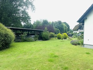 Une cour bien entretenue, avec une pelouse verdoyante, une pergola en bois, des arbustes taillés avec soin et un petit arbre.