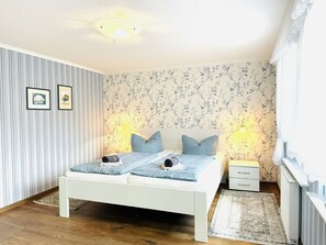 Une chambre avec un lit blanc, un papier peint à rayures, un papier peint à motifs floraux et un plancher en bois.