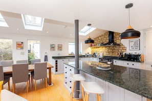 A modern kitchen with a central island, a dining area with chairs, and a view of the outdoors. - Spacious 3BD with Large Garden in Aynho (Banbury)