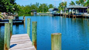 A wooden dock extending into calm water, surrounded by lush greenery and docked boats. - 4BR Waterfront Retreat - Private Dock, Kayaks, Hot Tub & Tiki Bar  Walk to Beach (Cocoa Beach)