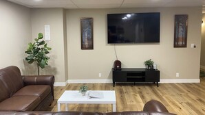 Una sala de estar con un sofá de cuero marrón, una mesa de centro blanca, un televisor de pantalla plana montado en la pared y un mueble negro para equipo multimedia.
