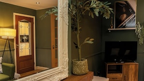 Ein Wohnzimmer mit einem großen Spiegel, einem Blumentopf, einem Fernseher und einem Holzschrank.