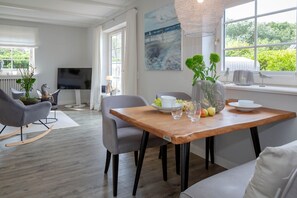 Una sala de estar moderna con comedor, que incluye una mesa de madera, sillas grises, un sofá y un televisor al fondo.