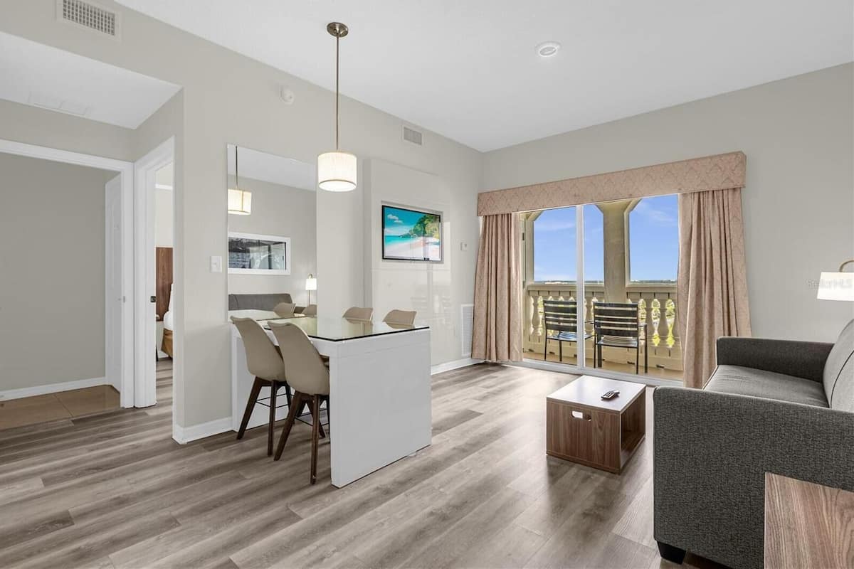 A modern living room with a dining area, large windows with curtains, and a balcony with outdoor furniture.