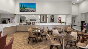 Ein geräumiger Essbereich mit mehreren Tischen und Stühlen, eine Küche im Hintergrund und ein großes Gemälde an der Wand.