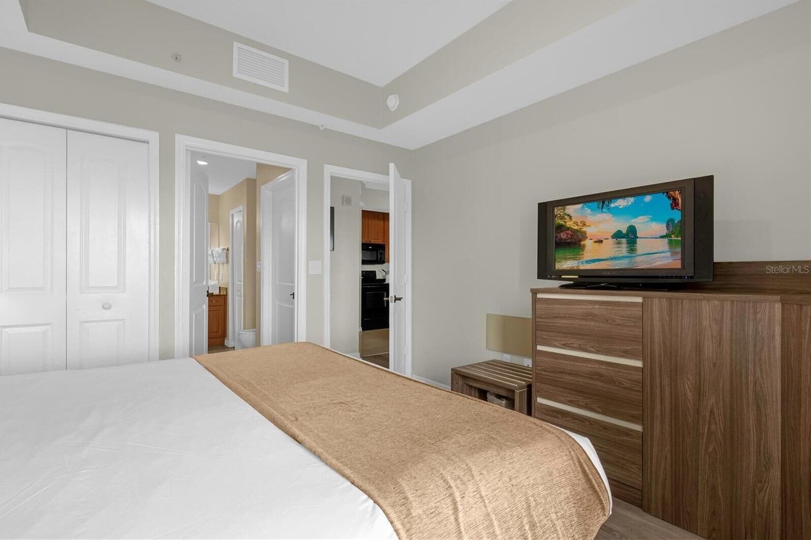 Ein Hotelzimmer mit einem Bett, einem Fernseher auf einer Holzkabine und Blick auf die Küche durch eine offene Tür.