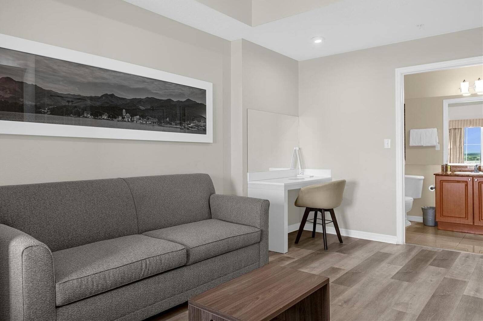 A modern living room with a grey sofa, a wooden coffee table, a white desk, and a chair.