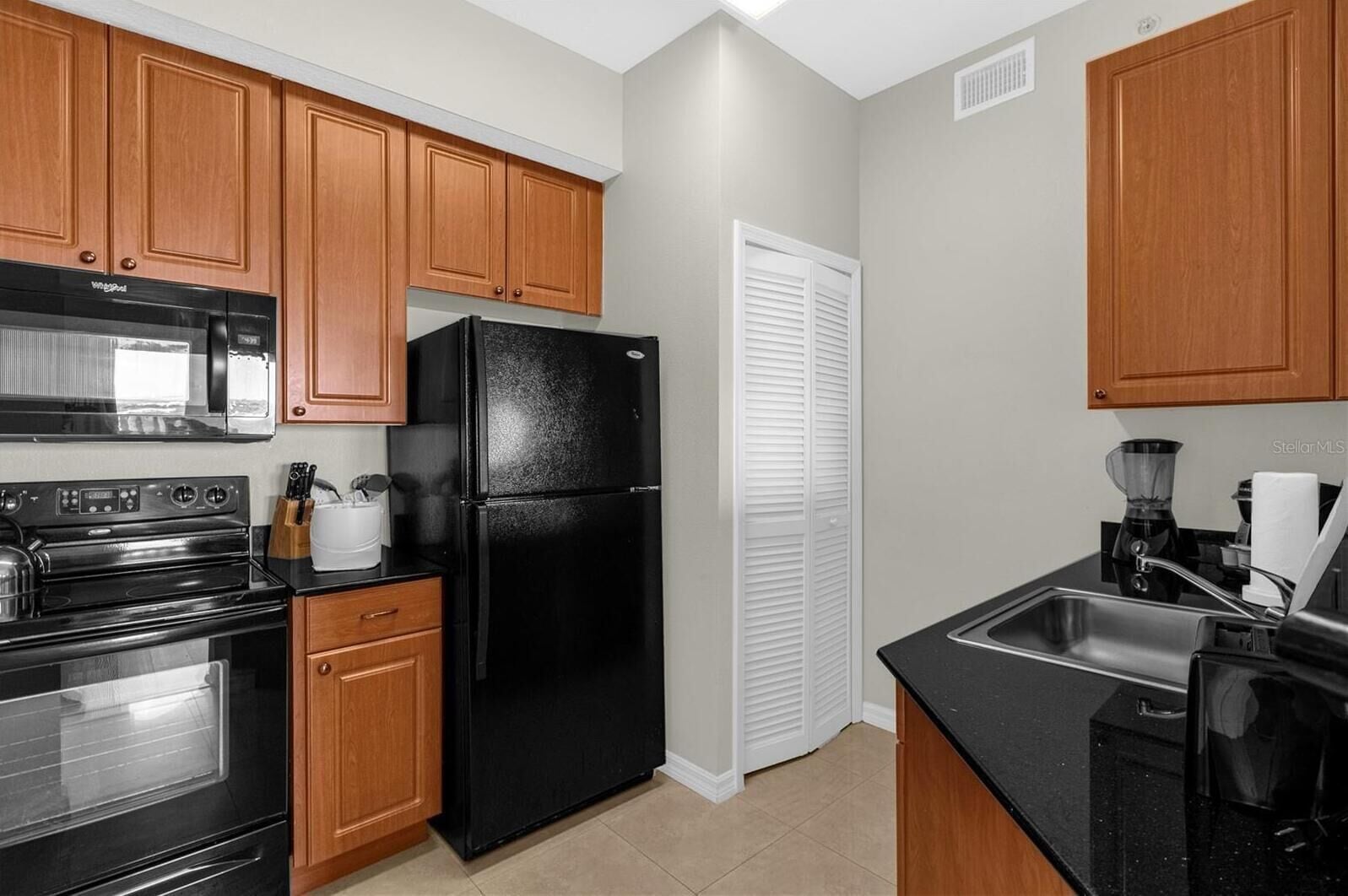 A kitchen with wooden cabinets, a black refrigerator, a stove, and a sink.