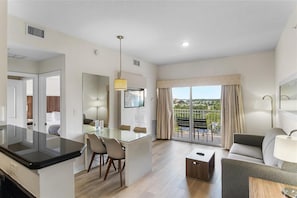 A modern hotel room with a dining area, a sofa, a balcony with curtains, and a large window.