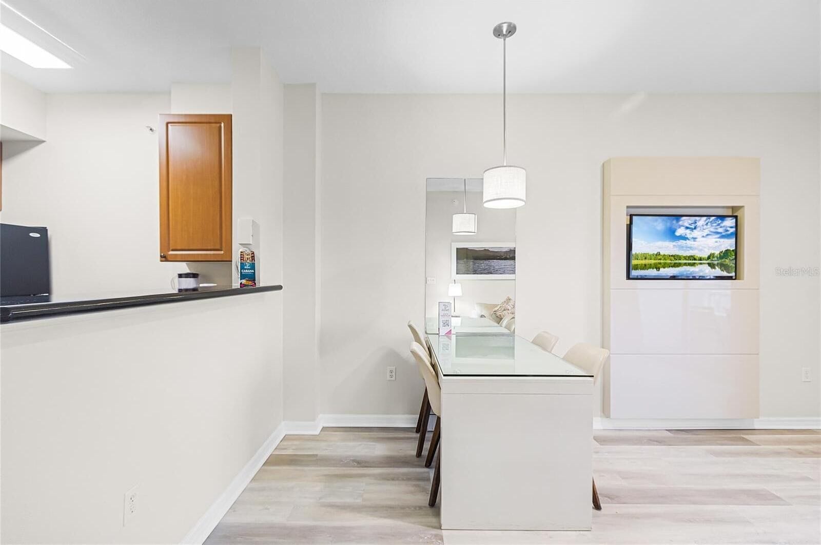 A modern kitchen with a central island, a dining area with a glass table, and a living space with a TV and a view of a lake.