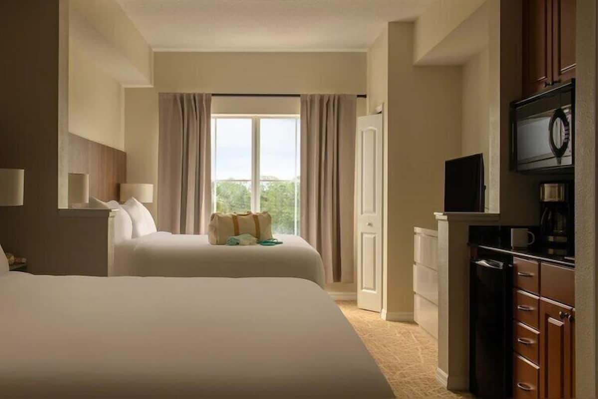 A hotel room with two beds, a TV, a desk, and a window with curtains.