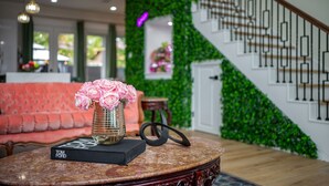 Een ronde tafel met een boek getiteld 'Tom Ford' en een vaas met roze bloemen, een rode bank en een trap met een groene wand.