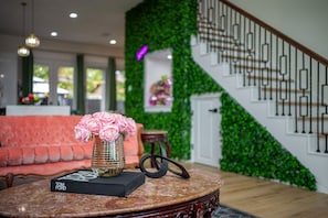 A round table with a book titled 'Tom Ford' and a vase with pink flowers, a red sofa, and a staircase with a green wall.