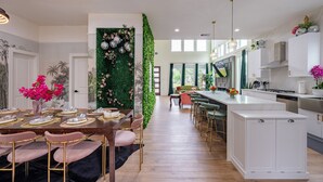 Een moderne keuken met witte kastjes, een centraal eiland en een eetgedeelte met een lange tafel en stoelen.