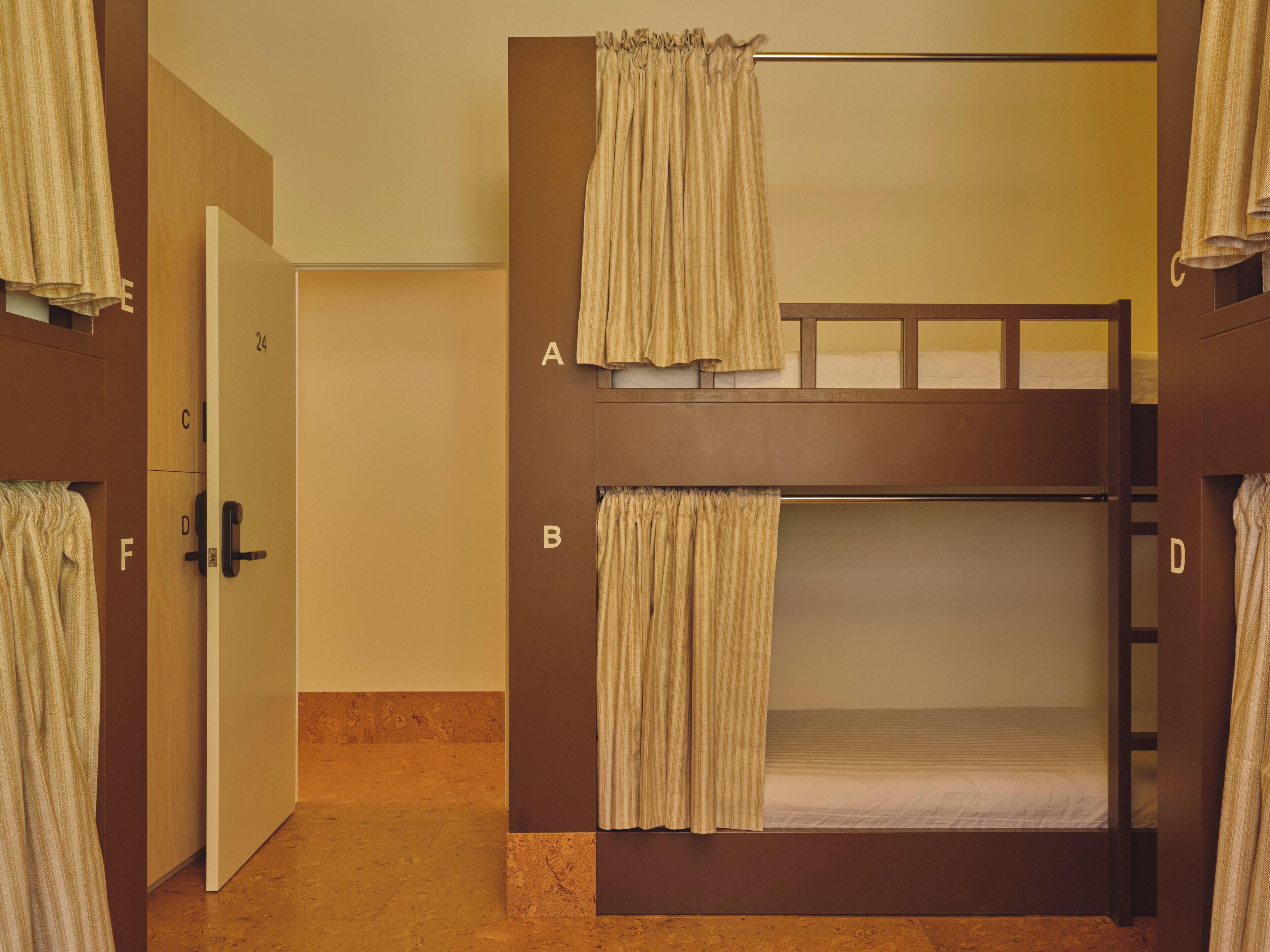 Une chambre avec un lit superposé, une porte portant l’inscription « 24 » et une armoire avec un miroir.