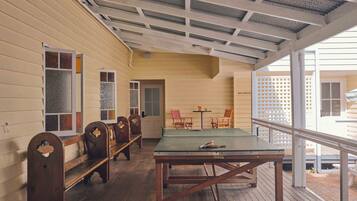 A covered porch with wooden benches and a ping pong table, a door leading to a bathroom, and a view of the outside.