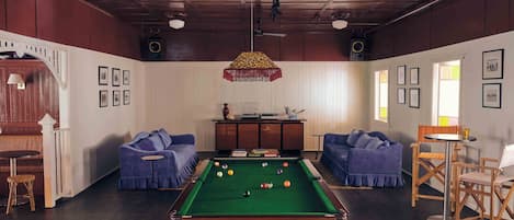 A pool table in a room with two sofas, a small table with chairs, and framed pictures on the walls.