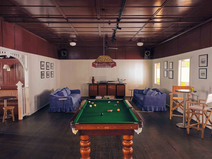 A pool table in a room with two sofas, a small table with chairs, and framed pictures on the walls.