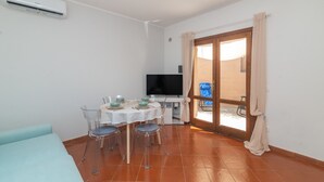 A room with a dining table, chairs, a TV, and a sliding glass door to the outside. - Apartment 'Relax Porto Mannu' with Sea View, Wi-Fi and Air Conditioning (Palau)