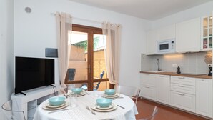 A dining area with a table set for four, a flat-screen TV, and a kitchen with white cabinets and a microwave. - Apartment 'Relax Porto Mannu' with Sea View, Wi-Fi and Air Conditioning (Palau)