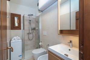 Un baño moderno con cabina de ducha de vidrio, inodoro, lavabo y espejo.