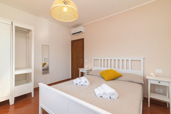 Una habitación de hotel con cama, armario, mesita de noche, lámpara y aire acondicionado.