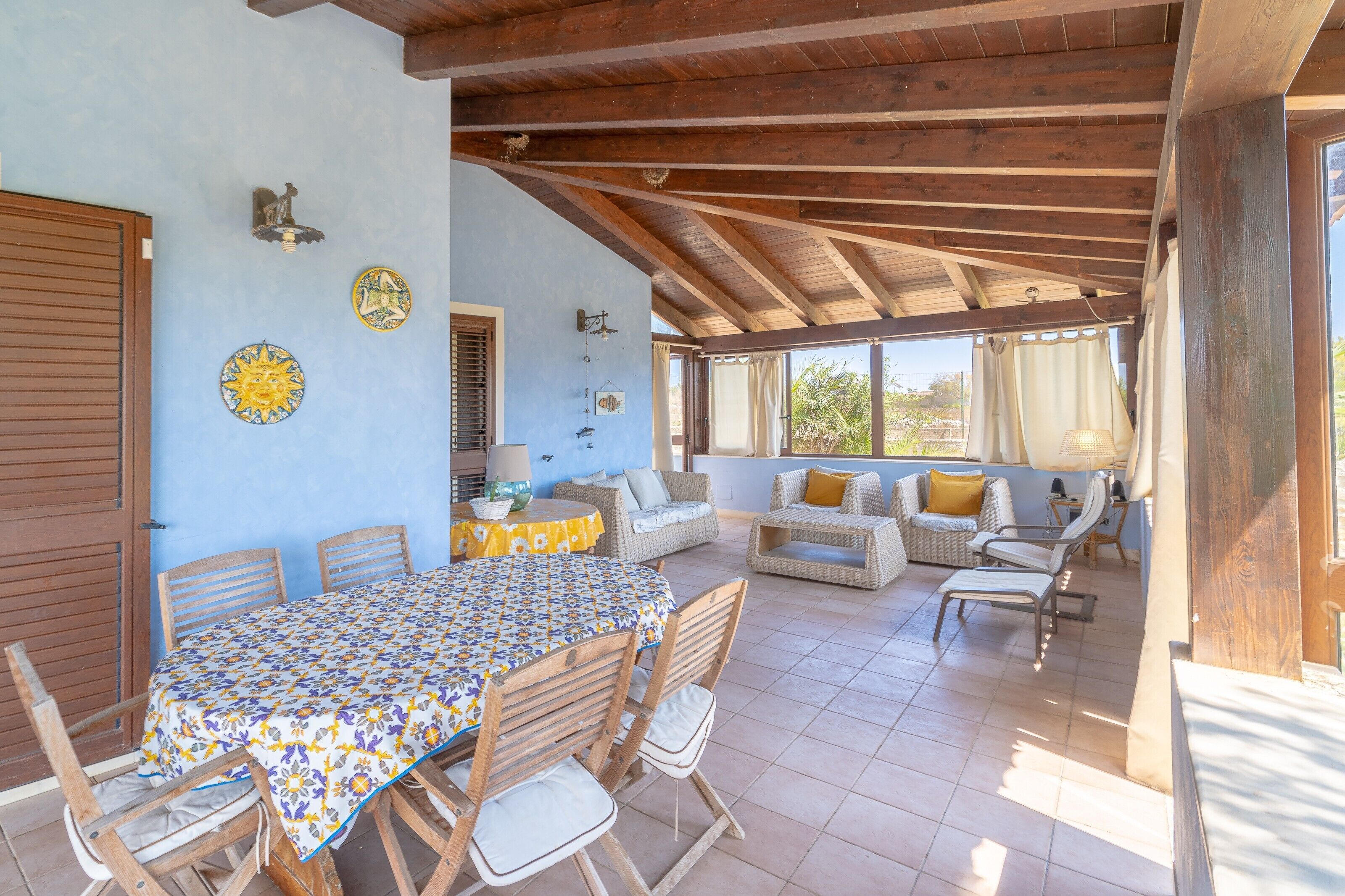 A covered patio with a dining table, chairs, and a sofa with cushions.
