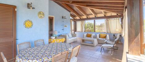 A covered patio with a dining table, chairs, and a sofa with cushions.