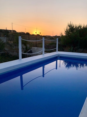 A swimming pool with a white deck and a view of the sunset in the background.