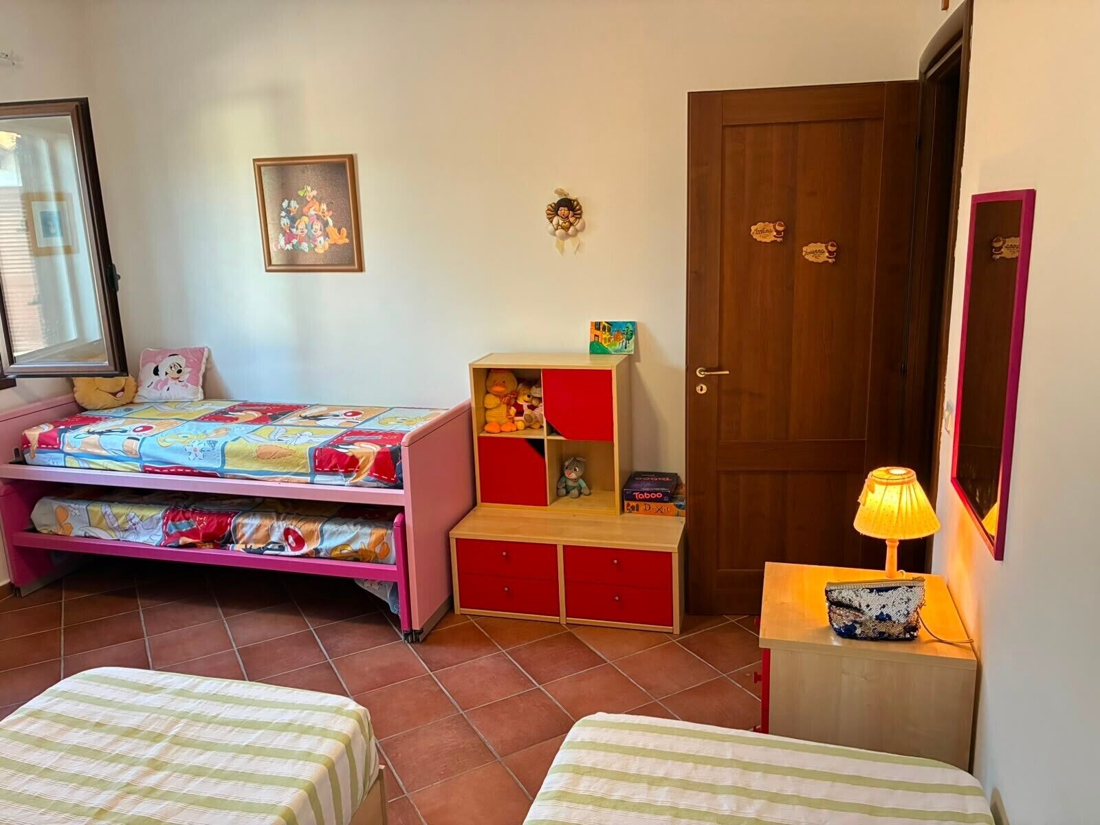 A child's bedroom with a bed, a small desk, a chair, a door, and a window.