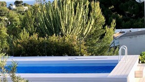 Een zwembad met helderblauw water, een trap naar een overdekt terras en enkele ligbedden.