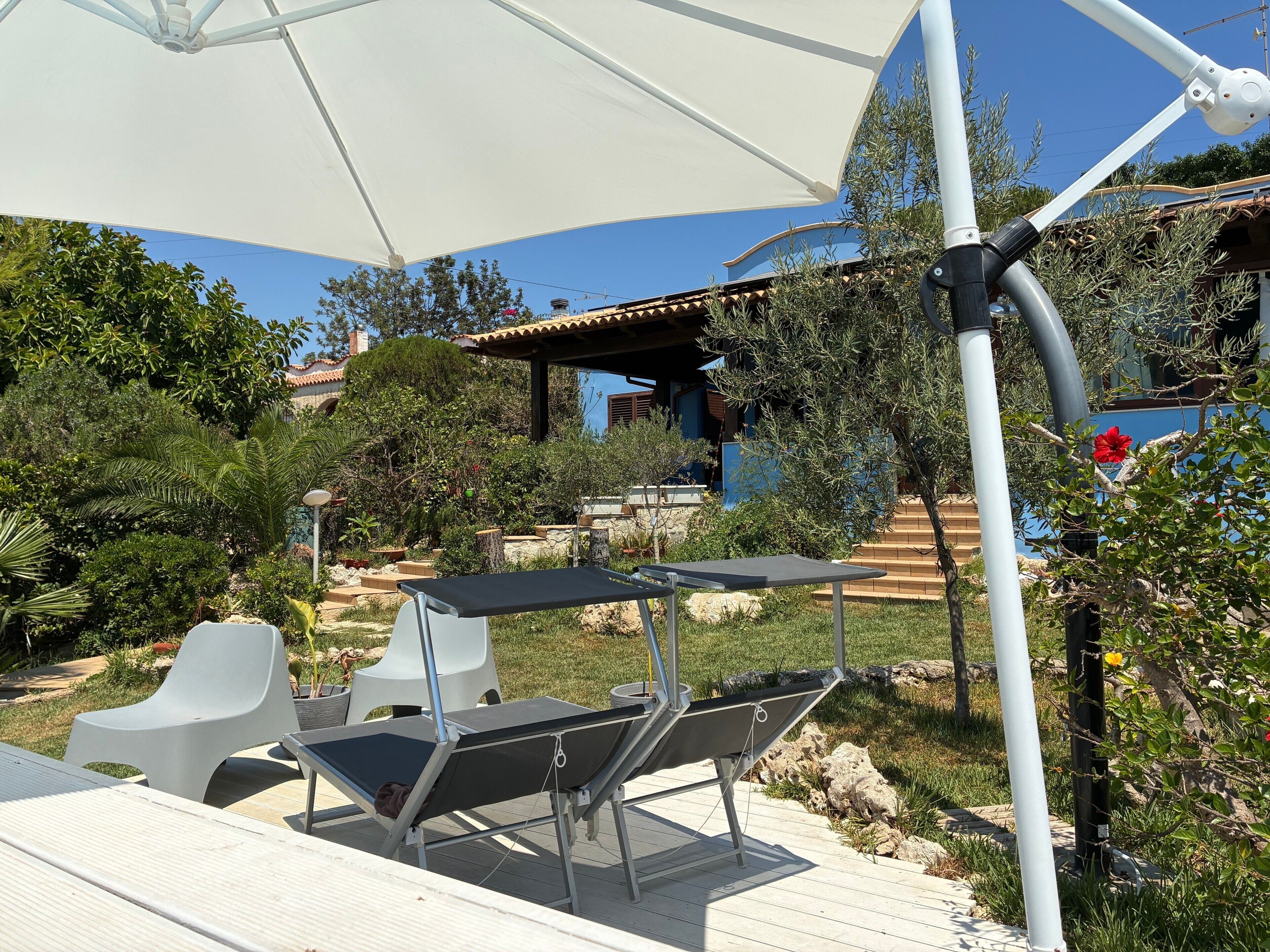 A patio area with outdoor furniture, a white umbrella, and a view of a building with a tiled roof.