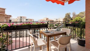 Un balcon avec une table et des chaises, un auvent rouge et des plantes en pot.