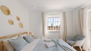 A bedroom with a bed, a chair, a window with curtains, and wall decorations.