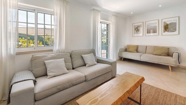 A modern living room with two sofas, a wooden coffee table, and large windows with curtains.