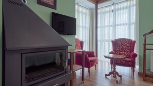 Uma sala de estar com lareira preta, uma televisão na parede, uma poltrona vermelha e uma mesa de madeira.
