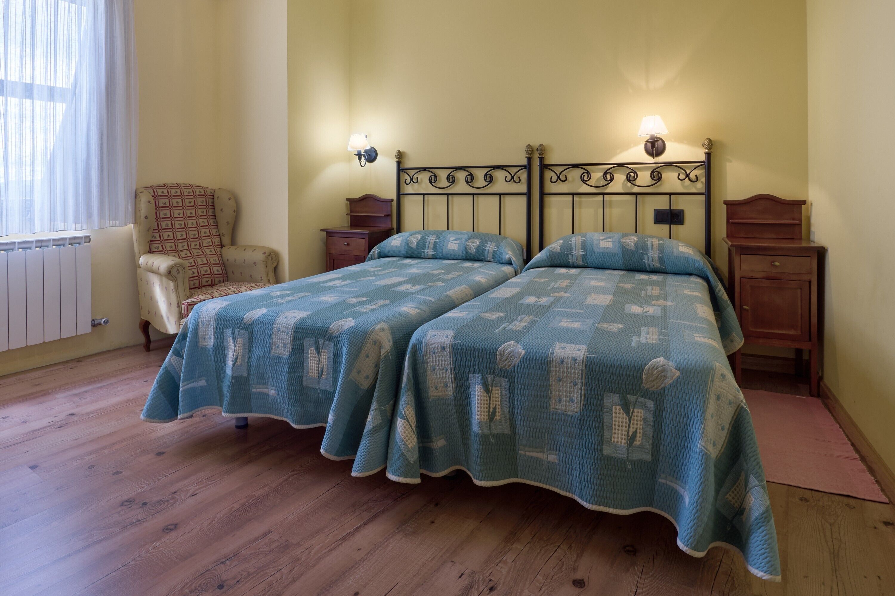 Un lit double avec une couvre-lit à motifs, deux tables de chevet avec des lampes, une chaise et un radiateur.