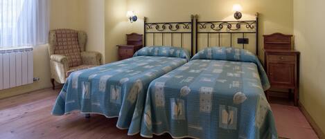 Un lit double avec une couvre-lit à motifs, deux tables de chevet avec des lampes, une chaise et un radiateur.