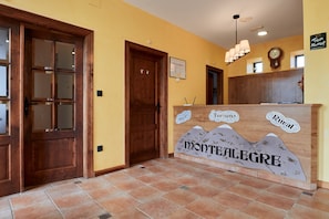 Una mesa de recepción con un cartel que dice 'Montealegre', una puerta de madera y un reloj fijado a la pared.
