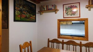 A dining area with a wooden table and chairs, a painting, a bookshelf, and a framed picture. - Holiday Home 'La Casa De Luis' with Mountain Views, Private Terrace and Wi-Fi (Castiello De Jaca)