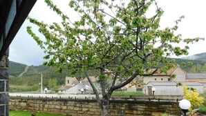 A stone wall, a tree, and a grassy area with a view of buildings in the background. - Holiday Home 'La Casa De Luis' with Mountain Views, Private Terrace and Wi-Fi (Castiello De Jaca)
