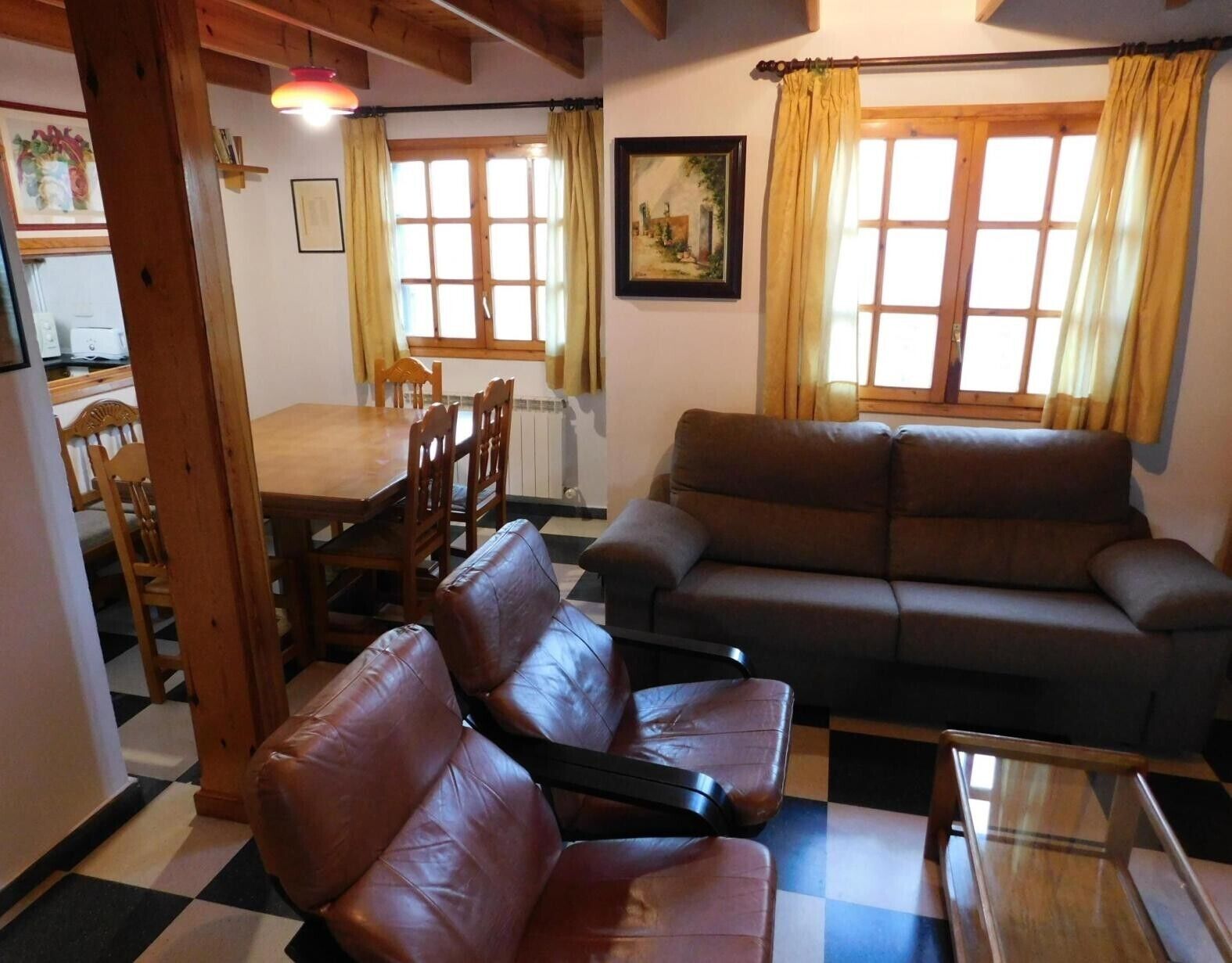 A living room with a sofa, a dining table with chairs, and a window with curtains.